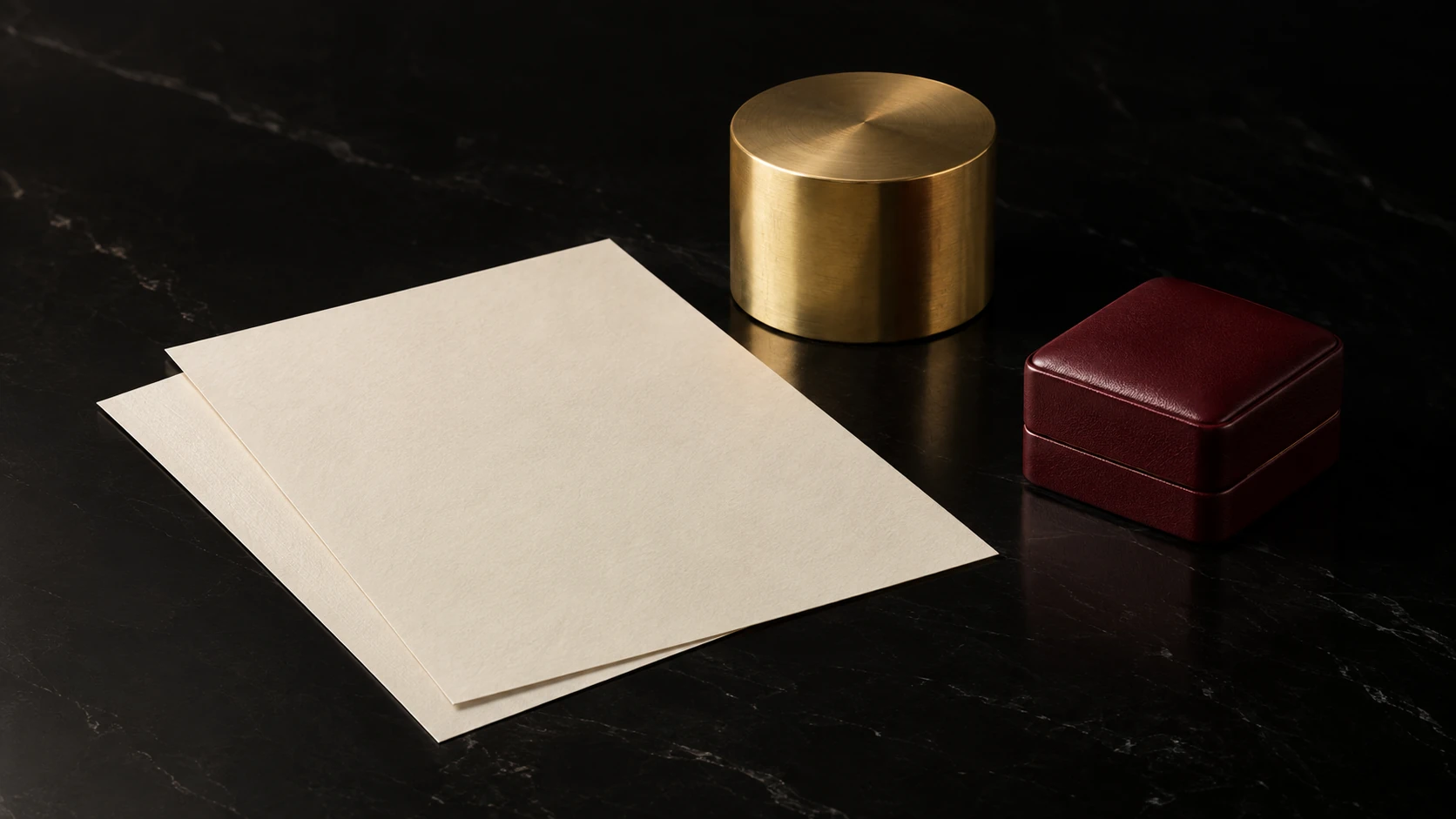 Clear expectations — premium black still life of two plain ivory paper sheets without print, unbranded brass deskweight shaped as smooth cylinder, small closed burgundy jewellery box
