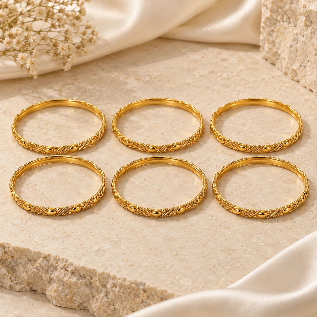 Bangles & Bracelets collection - exactly six separate matching narrow round gold bangles in a gentle staggered stack, each with small raised oval bosses alternating with fine diagonal milgrain lines, smooth inner bore